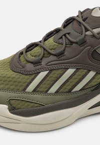 Olivgrön sportskor med texturerat tyg, läderdetaljer, tvåfärgade snören och kontrasterande tanfärgad sula med varumärkesdetalj.