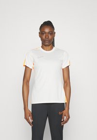 Niiskust eemaldas valge sport T-särk, millel on oranžid detailid varrukatel ja õlgadel. Rinnal on väike lilla Nike logo.
