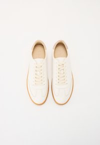 Sneakers color crema con una toma in pelle liscia, lacci piatti e suola in gomma beige. Presentano cuciture sottili e un design della punta arrotondata.