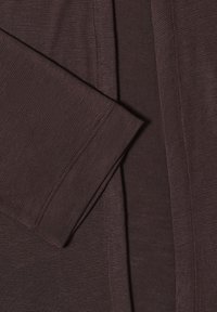Gros plan d'un tissu côtelé marron foncé avec des coutures visibles sur la manche pliée et la couture du corps du vêtement.