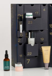 Kalendarz adwentowy w ciemnoniebieskim kolorze ze złotymi cyframi; zawiera różne produkty pielęgnacyjne: serum, nawilżacze oraz tonik, o różnych kształtach i rozmiarach.