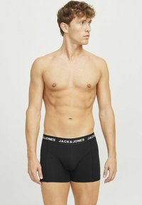 Boxer en coton noirs avec une ceinture logo blanche, design ajusté et longueur mi-cuisse, portés par un modèle.