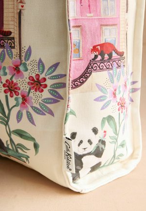 Beeži kangast koti nurk lilleliste mustritega, panda hoiab bambust ja punane panda rõdul roosade akende all.