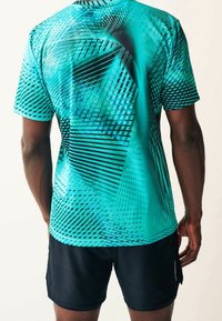 Camiseta activa de manga corta en color verde azulado con patrones geométricos y líneas negras; combinada con pantalones cortos negros; tela suave y ligera.