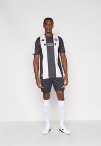 Sort-hvidstribet kortærmet fodboldtrøje med "MAXBET"-branding, kombineret med sorte shorts, hvide sokker og hvide fodboldstøvler.