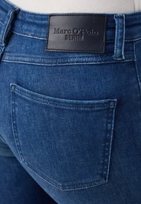 Jeans de mezclilla azul oscuro con una textura suave, que cuentan con un parche de cuero etiquetado "Marc O'Polo DENIM" en la cintura y un bolsillo trasero.