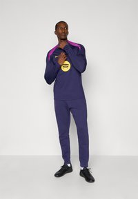 Purple athletic set featuring a long-sleeve shirt with a yellow Spotify logo and pink accents, paired with matching fitted pants and black shoes.