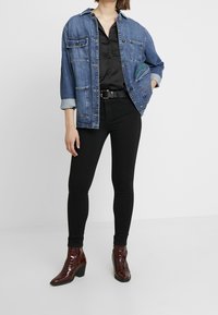 Denim jacket with two front pockets, button closure, rolled sleeves; worn over a black top and paired with black skinny jeans and burgundy ankle boots.