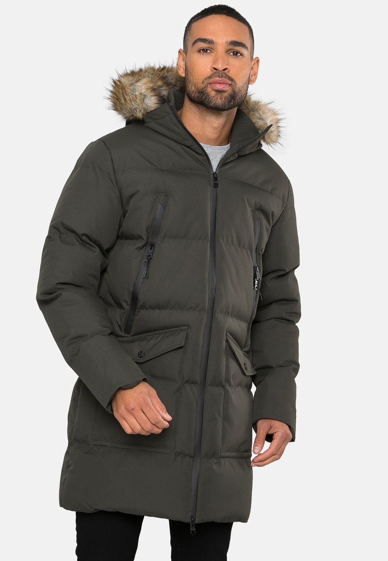 Gewatteerde parka jas in donkergroen, met een met bont gevoerde capuchon, ritszakken op de borst en knoopzakken aan de voorkant. Zachte, gewatteerde textuur.