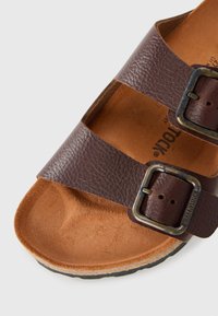 Barna bőr szandál, két állítható csat segítségével és formázott parafa talppal, közelről a frontja és az oldala.