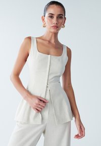 Lichtbeige getailleerde top met een vierkante halslijn, een ritssluiting aan de voorkant, een peplum ontwerp en zonder mouwen, gecombineerd met bijpassende brede broekspijpen.