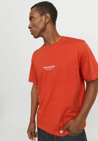 Rotes Baumwoll-T-Shirt mit Rundhalsausschnitt und kurzen Ärmeln, mit einem weißen "Originals Studio"-Logo auf der Brust.