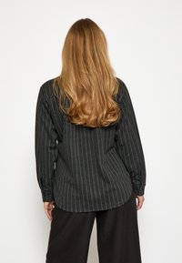 Camicia a maniche lunghe a righe bianche e nere con orlo arrotondato e polsini con bottoni, realizzata in un tessuto dalla texture liscia.