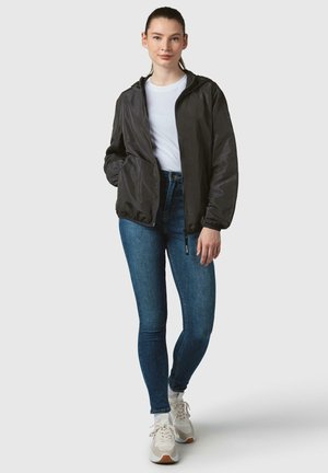Svart, zippered bomberjacka med huva och elastiska manschetter, bärs över en vit t-shirt. Kombination med blå skinny jeans och ljusa sneakers.