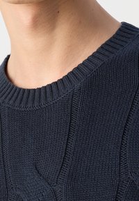 Zone du cou et des épaules portant un pull tricoté bleu foncé avec un col côtelé et un motif torsadé.