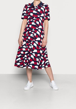 Femme portant une robe courte à manches courtes avec un motif abstrait bleu marine, rouge et blanc et des baskets blanches.