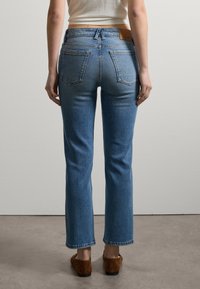 Hochtaillierte blaue Denim-Jeans mit geradem Schnitt, fünf Taschen und einem Lederpatch am hinteren Bund. Enthält braune Clogs.