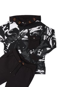 Zwart-witte grafische hoodie met een voorzak en bruine accenten, gecombineerd met zwarte sweatpants met een elastische tailleband en trekkoord.