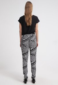 Black short-sleeve top paired with black and white patterned trousers featuring zigzag and geometric designs. Model stands with back to camera.