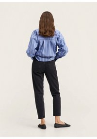 Camisa a rayas azul con mangas largas, jeans negros ajustados y zapatos negros planos, vista desde la parte de atrás. Tela suave, corte casual.