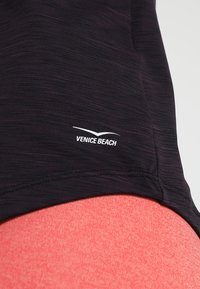 Musta urheilu paita, jossa on teksturoitu kangas, ja siinä on valkoinen "Venice Beach" -logo sivussa, yhdistettynä korallinvärisiin alaosiin.