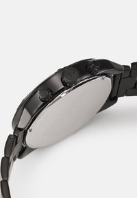 Montre chronographe noire avec un boîtier rond lisse et trois boutons ronds sur le côté. Bracelet en métal avec finitions brossées et polies.