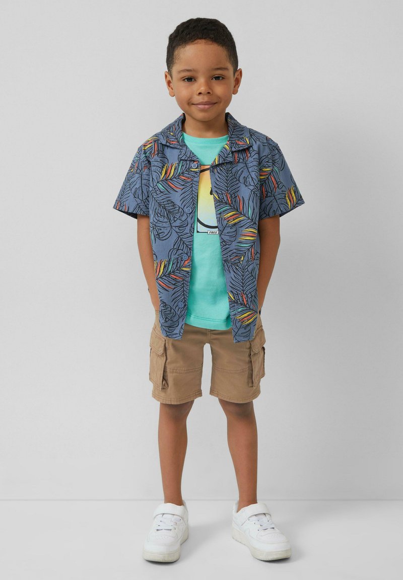 Korte mouwen, blauw gebloemd shirt met bladpatronen, groene T-shirt, beige cargo shorts en witte sneakers.