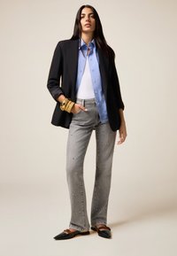 Blazer negro ajustado, camisa azul clara, top blanco, jeans grises con embellishments y bailarinas negras con acentos marrones, estilizadas con pulseras doradas.