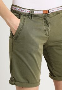 Shorts vert olive en mélange de coton, dotés de poches latérales, d'ourlets roulés et d'une ceinture décorative à motif avec un accent en cuir marron.