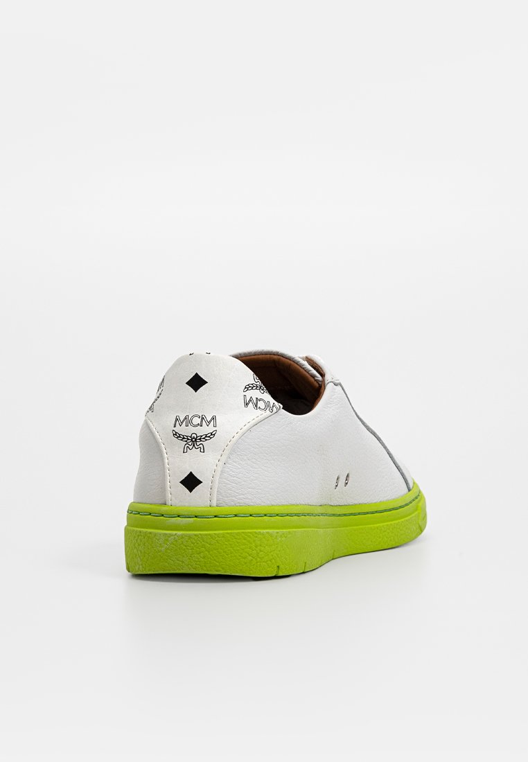 Weißes Leder-Sneaker mit grüner Gummisohle, ausgestattet mit schwarzen Logo-Details und einer glatten Textur; abgerundete Form mit minimaler Naht.