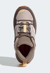 Hnědá textilní obuv s nylonovým svrškem, zdobená akcenty v žluté, šedé a bílé barvě, s polstrovaným límcem a texturovanou gumovou podrážkou.