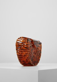 En handväska med sköldpaddsmönster och en unik flikformad design, tillverkad av transparent akryl, med en rundad silhuett och knäppning.