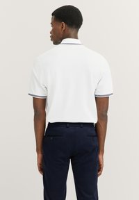 White polo shirt with a collar, featuring contrasting navy stripes at the cuff, paired with navy trousers, showcasing a tailored fit.