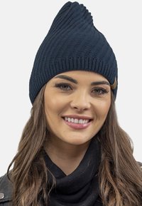 Căciulă tricotată de culoare bleumarin, cu un design ascuțit, având o textură cu nervuri verticale și un mic accent din piele maronie pe lateral.