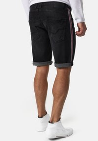 Shorts en denim noir avec une finition légèrement délavée, des ourlets roulés et des bandes latérales contrastantes en rouge, bleu et blanc. Deux poches arrière.