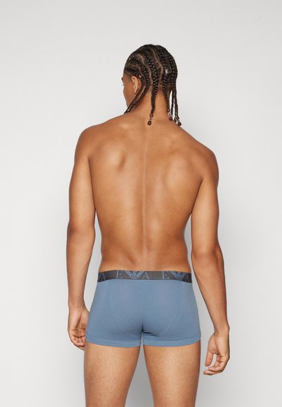 Boxer shorts azules ajustados con una cinturilla de logo negra, textura suave y un diseño sencillo, mostrados desde un ángulo trasero sobre un torso desnudo.