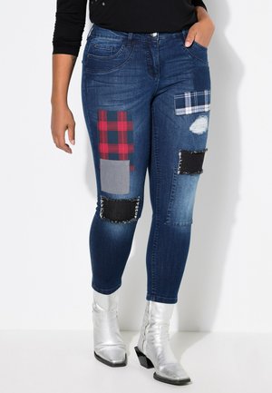 Jeans skinny di denim con toppe a quadri e colori solidi, caratterizzati da dettagli strappati e stivaletti metallici argento alla caviglia.