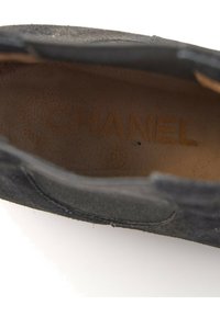 Vue intérieure d'une chaussure en suède noire avec le nom de la marque Chanel embossé sur la semelle intérieure en cuir beige.