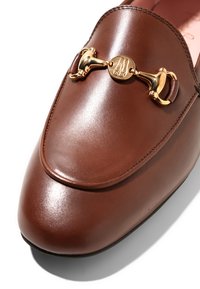 Mocassin en cuir marron avec détail mors d'or sur le dessus, doté d'une finition lisse et d'un design à bout arrondi.
