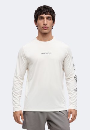 Mann trägt weißes langärmeliges ASICS FUJITRAIL Shirt mit schwarzem Text und Grafiken auf den Ärmeln, kombiniert mit grauen Shorts, steht frontal.