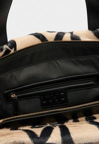 Interno della borsa nera con una tasca con zip e foderato in finta pelliccia beige con strisce nere a tigre.
