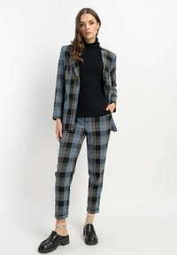 Kraciasty garnitur w odcieniach niebieskiego, czarnego i beżowego; smukła sylwetka z dopasowaną marynarką i skrojonymi spodniami; zestawiony z czarnym golfem.