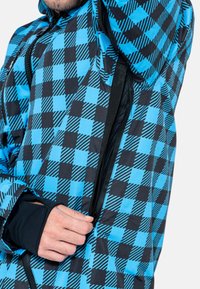 Chaqueta de cuadros azul y negro hecha de material ligero, con cremallera y orificios para el pulgar. Los patrones incluyen cuadrados sólidos y a rayas.