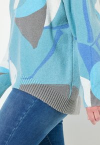 Ljusblå tröja med abstrakta grå och blå mönster. Ribbad i ärmslut och nederkant. Mjuk textur, avslappnad passform och sidofickor för ökad rörelsefrihet.