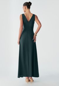 Pikk, tume roheline kleit, millel on V-kujuline tagakülg, varrukateta lõige, keha järgiv üleõlaosa ja voolav seelik. Sujuv kangas ilma nähtavate mustriteta.