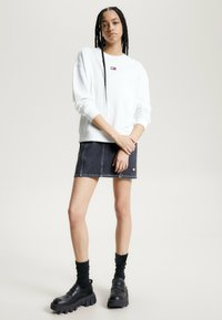 Felpa bianca con un piccolo logo, mini gonna in denim scuro e scarpe platform nere con suola spessa, abbinate a calze nere a costine.