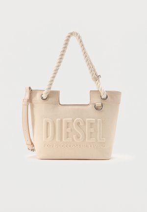 Μπεζ υφασμάτινη τσάντα Diesel με στριφτές λαβές από σχοινί, ανάγλυφο λογότυπο, ρυθμιζόμενο δερμάτινο λουρί και μεταλλική λεπτομέρεια δαχτυλιδιού σε απλό φόντο.