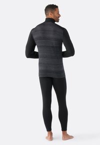 Haut de sport noir avec un dos texturé gris et des manches noires unies, associé à un pantalon noir ajusté, conçu pour une utilisation en tenue de sport.