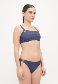 Marineblauw bikini van een textuurstof, rechthoekige bovenbanden met ronde hardware en bikinibroekjes met strikjes aan de zijkant.