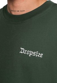 Mørkegrøn bomulds T-shirt med hvidt broderet "Dropsize" tekst, rund halsudskæring og glat tekstur.